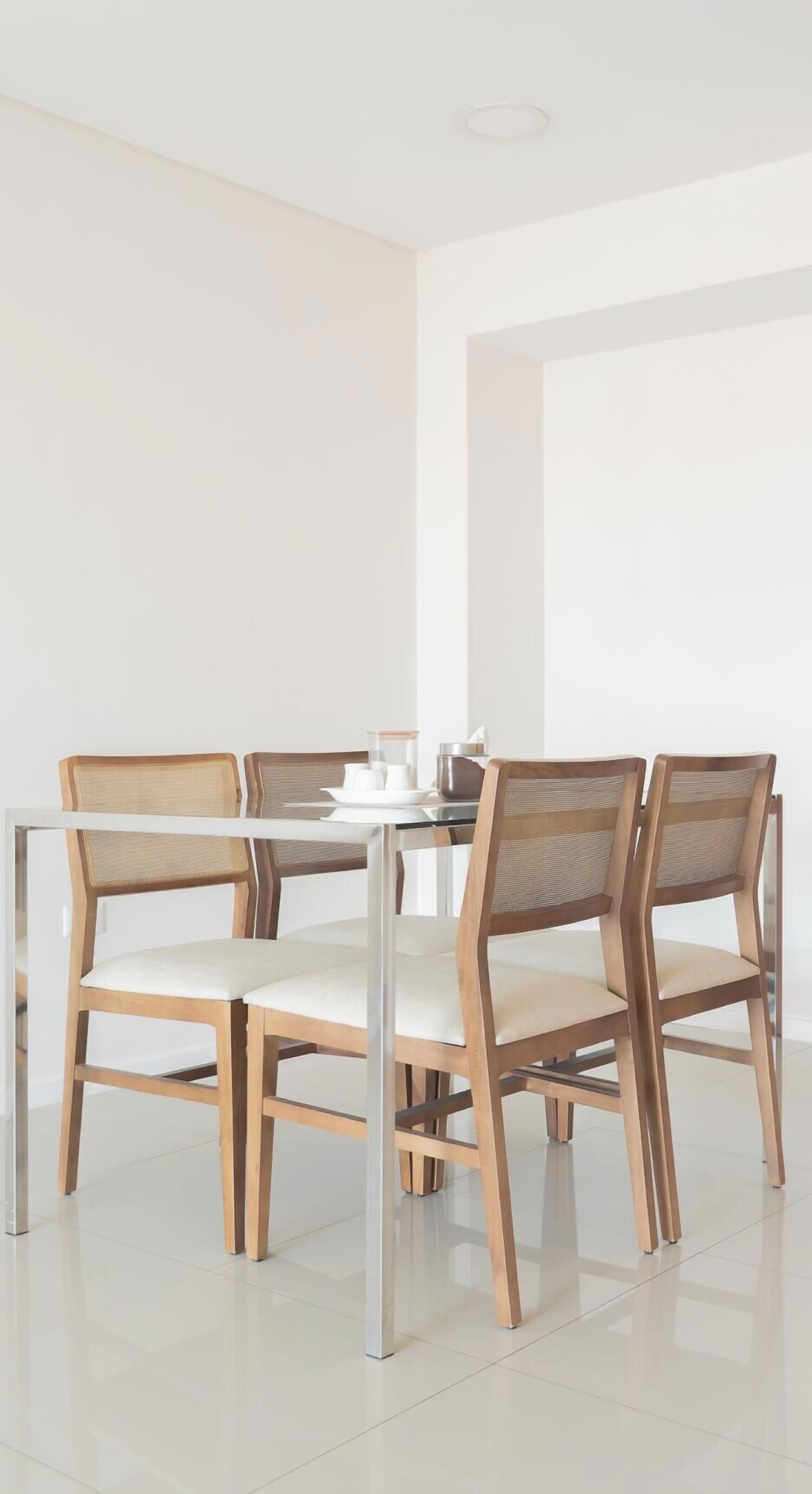 A dining area with a glass table surrounded by four wooden chairs with cushioned seats.