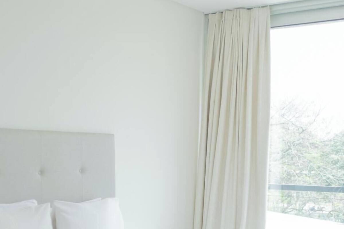 A hotel room with a large bed, a headboard, and a window with curtains.