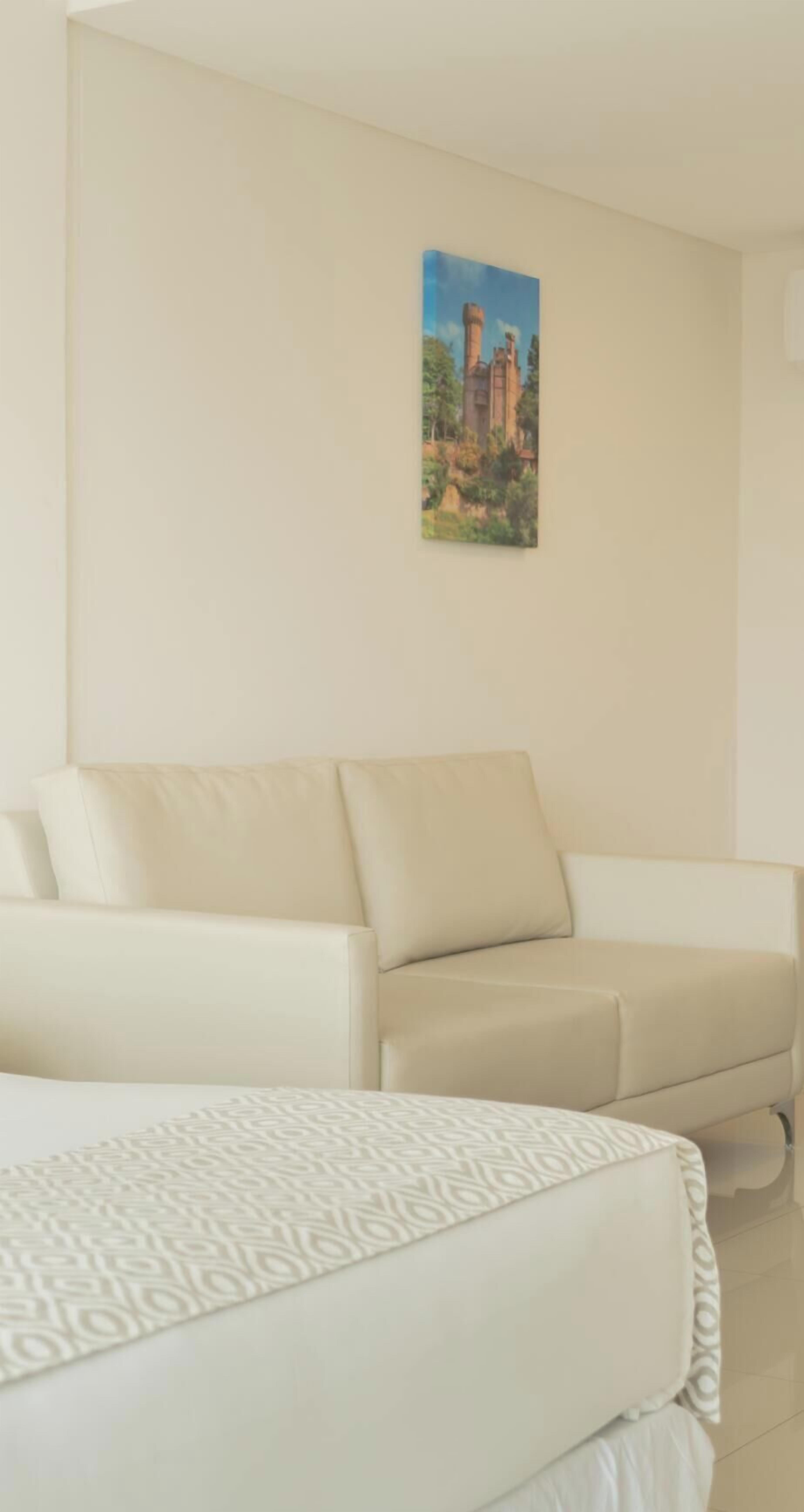 Hotellihuone, jossa on sänky, sohva ja taulu seinällä.