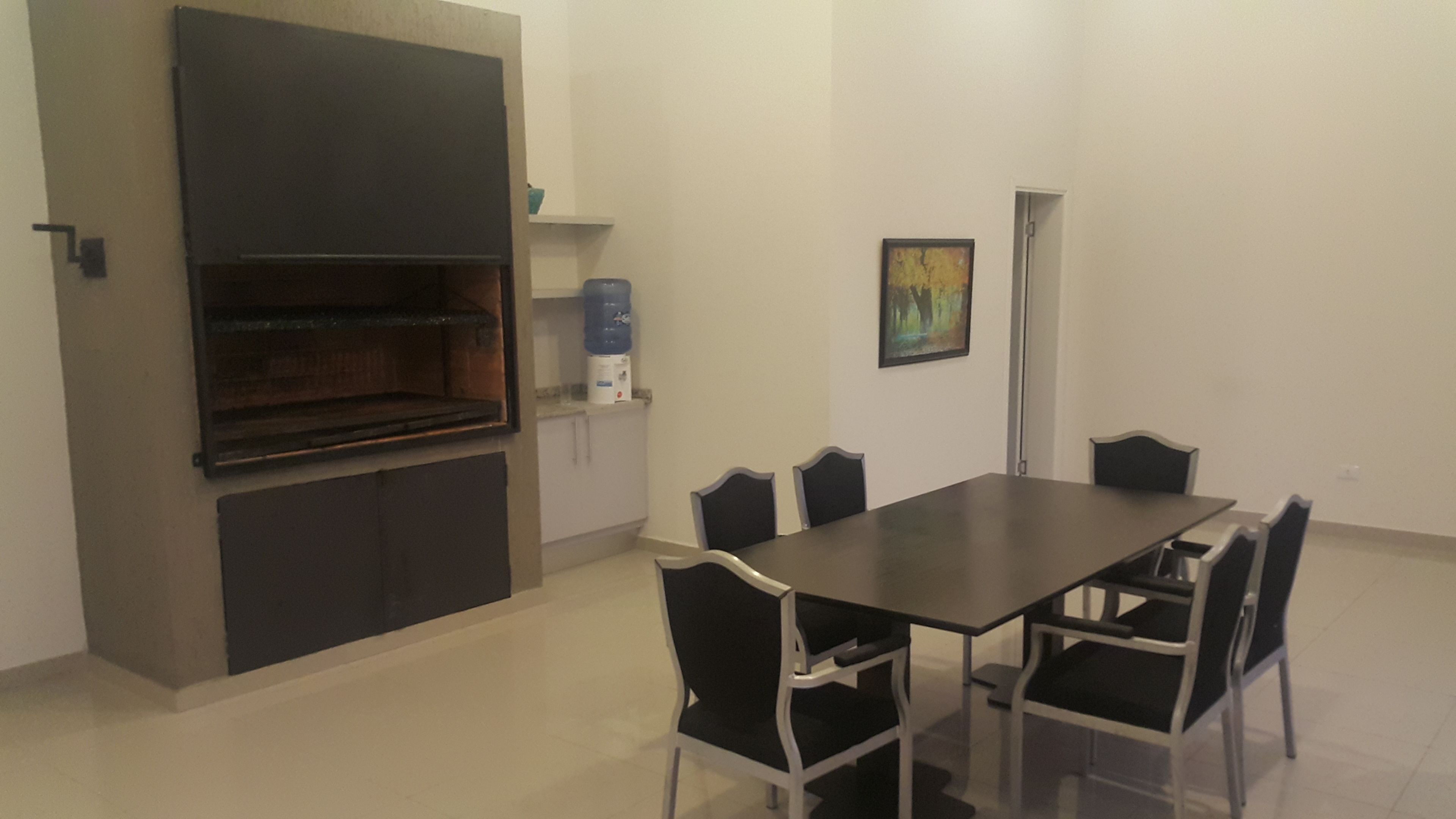 Un comedor con una mesa rectangular y seis sillas, un dispensador de agua y un cuadro en la pared.