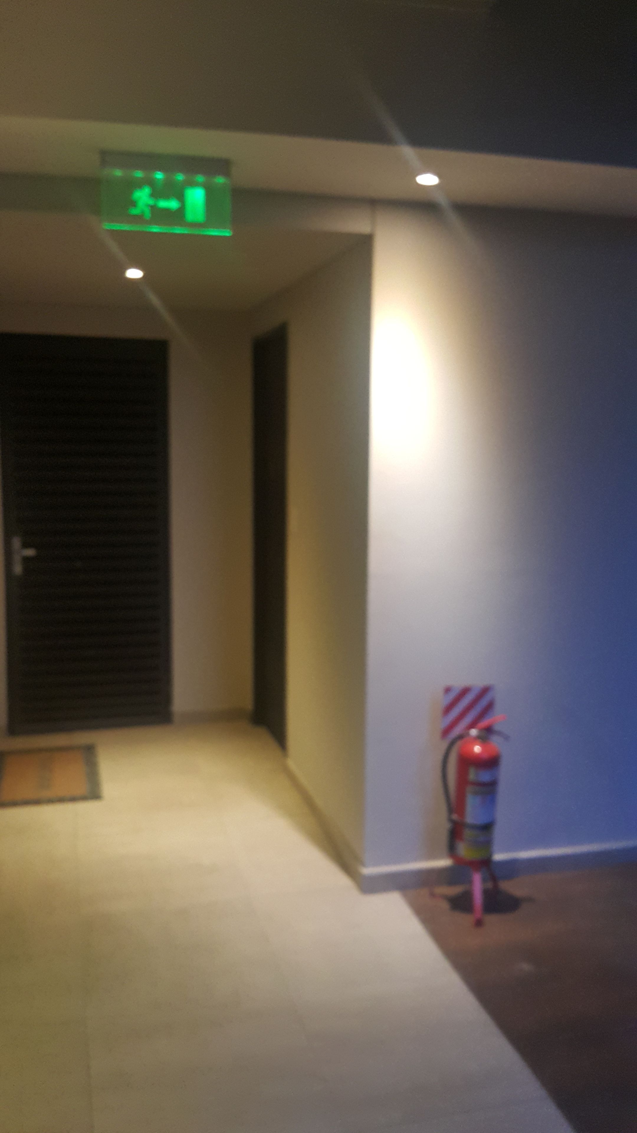 Un pasillo con un extintor montado en la pared y una pantalla digital sobre la puerta.