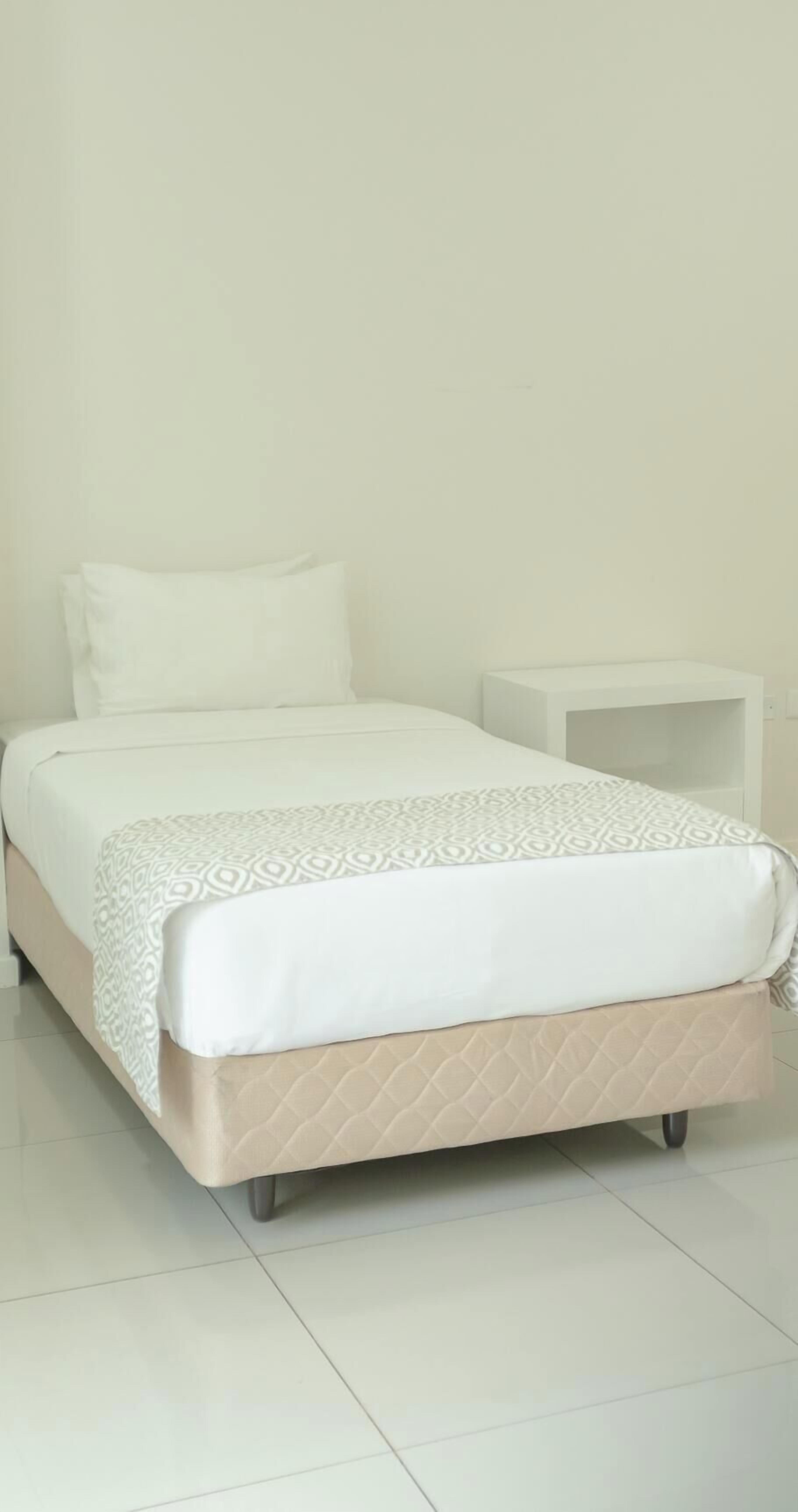 A bed with a patterned bedspread, a plain pillow, and a small bedside table.