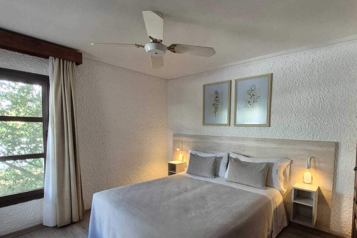 Une chambre avec un grand lit, deux tables de chevet, un ventilateur de plafond et une fenêtre avec des rideaux.