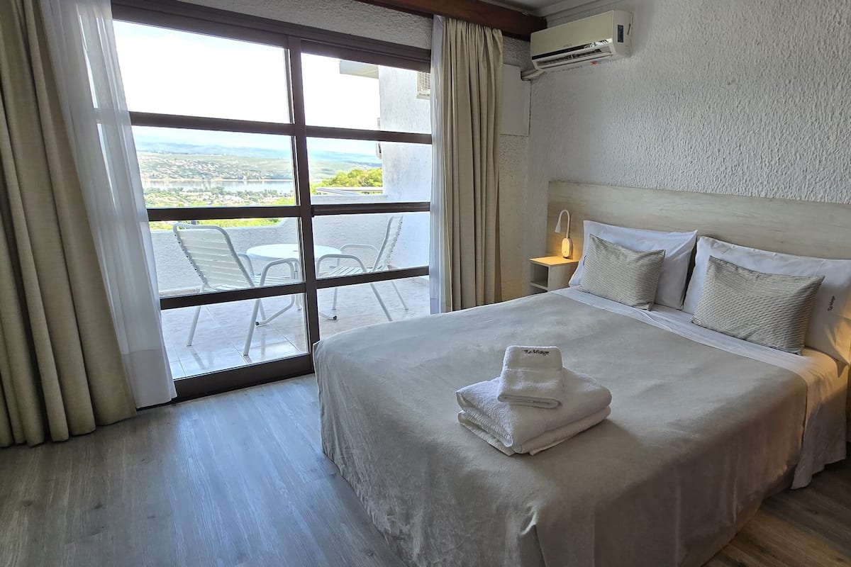 Une chambre d’hôtel avec un grand lit, une vue par la fenêtre et une table de chevet avec une lampe.