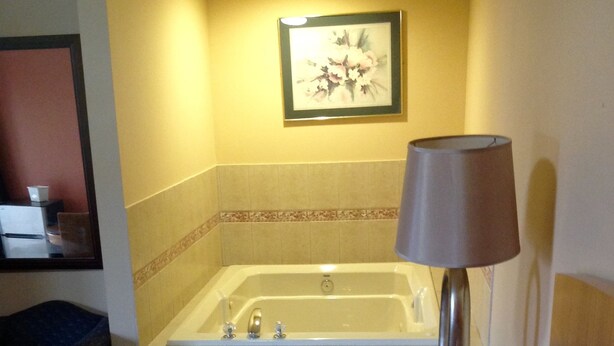 A hotel room with a large bed, a bathroom with a bathtub, a small table with a lamp, and a framed picture on the wall. - Sunset Motel (Egg Harbor Township)