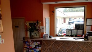 A reception desk with a window view of parked cars outside. - Sunset Motel (Egg Harbor Township)