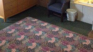 A hotel room with a wooden wardrobe, a television, a chair, a small trash bin, and a patterned bedspread. - Sunset Motel (Egg Harbor Township)