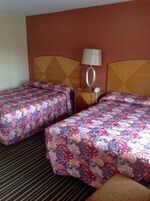 Habitación de hotel con dos camas, cada una con una colcha estampada, cabecero de madera, mesita de noche con lámpara y teléfono.