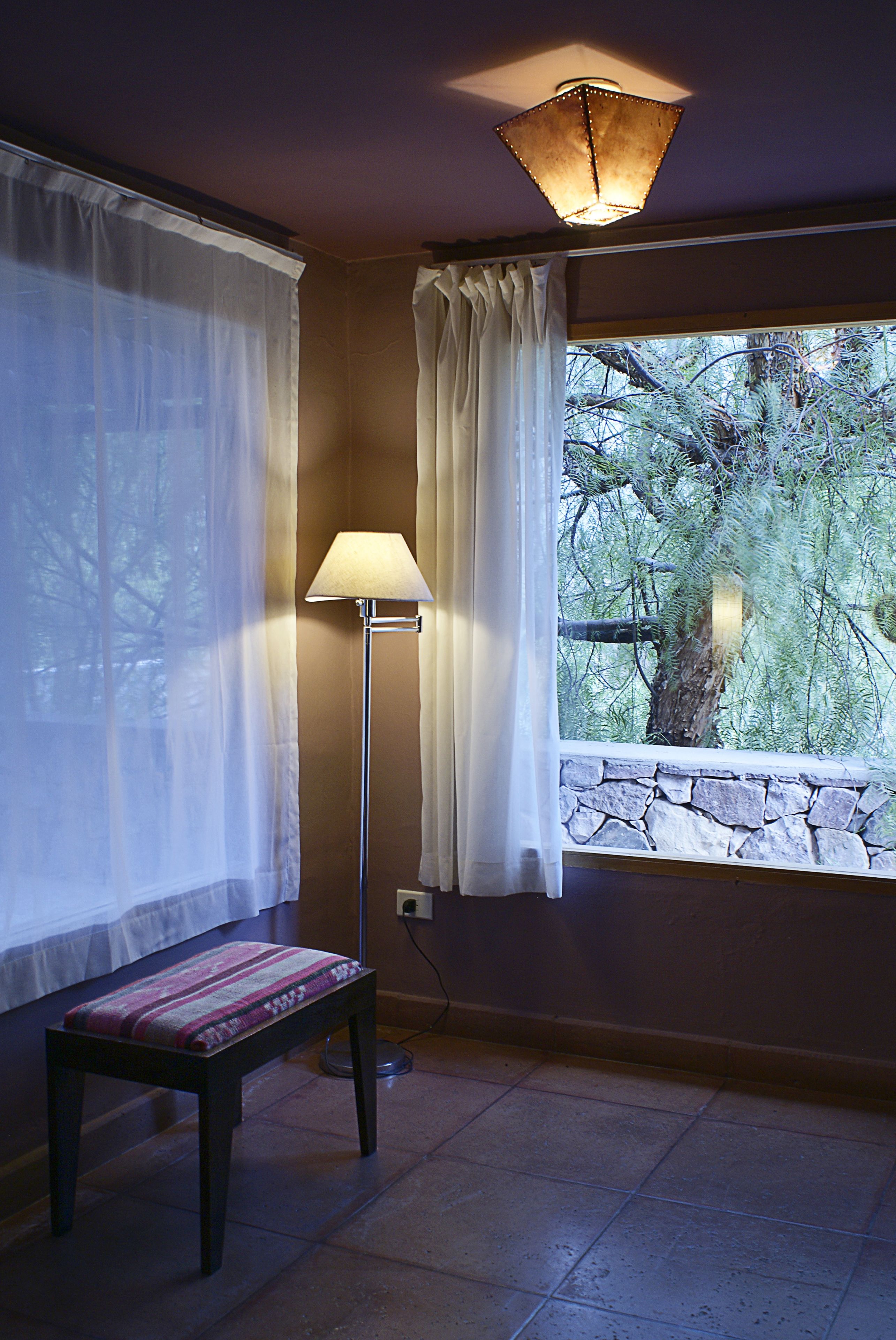A room with a stone wall, a bench, a floor lamp, and a window with curtains.