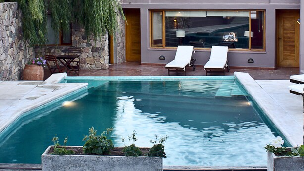 Uma casa moderna com piscina, duas cadeiras de descanso e um muro de pedra.