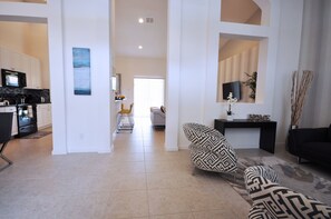 A modern living room with a patterned sofa, a black coffee table, and a black leather couch. There is a kitchen area with white cabinets and a black microwave. A dining area with a white table and chairs is visible in the background. - Solterra Resort by VHC Hospitality (Davenport)