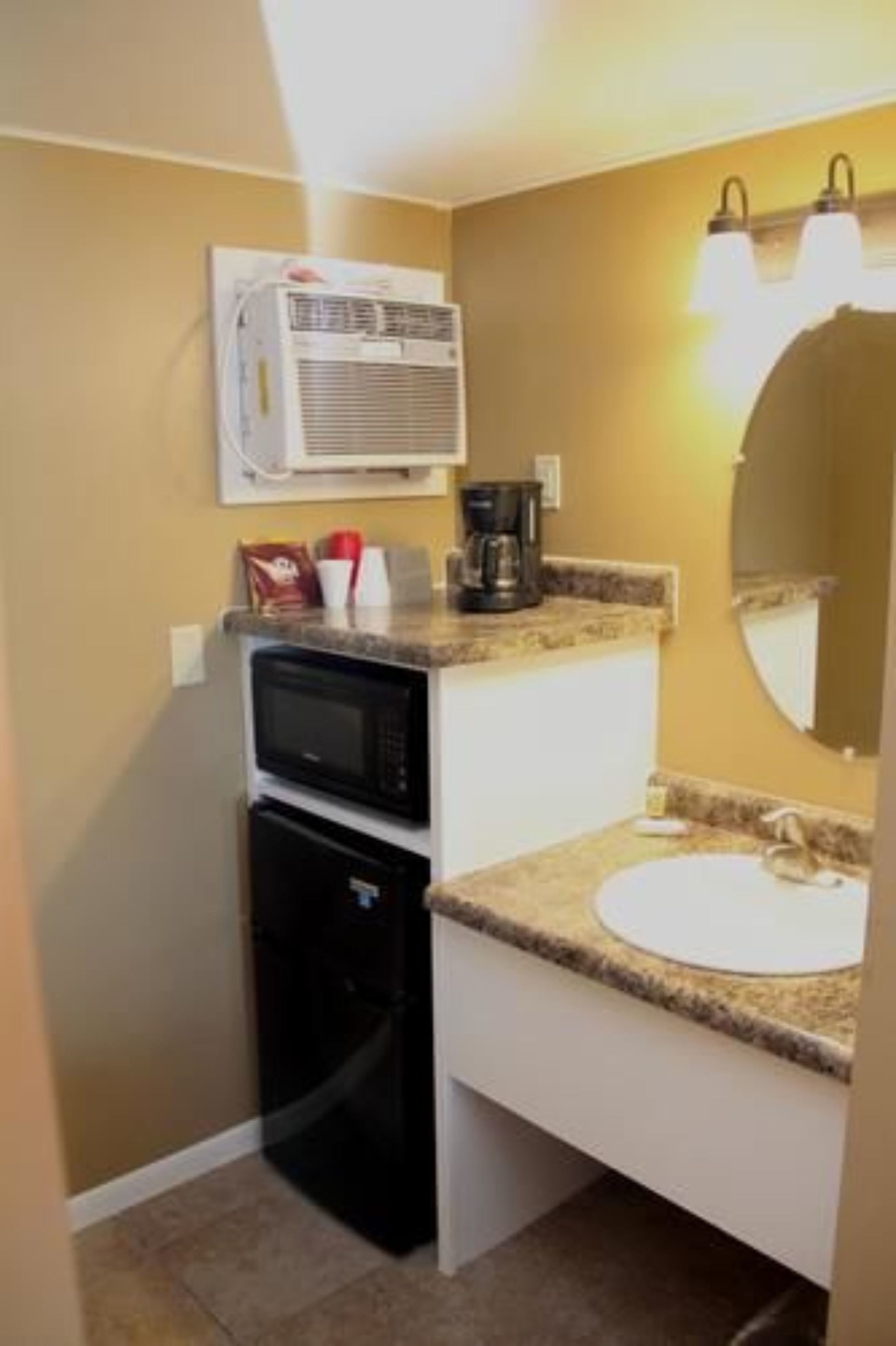 A compact bathroom with a sink, a microwave, a coffee maker, and an air conditioning unit mounted on the wall.