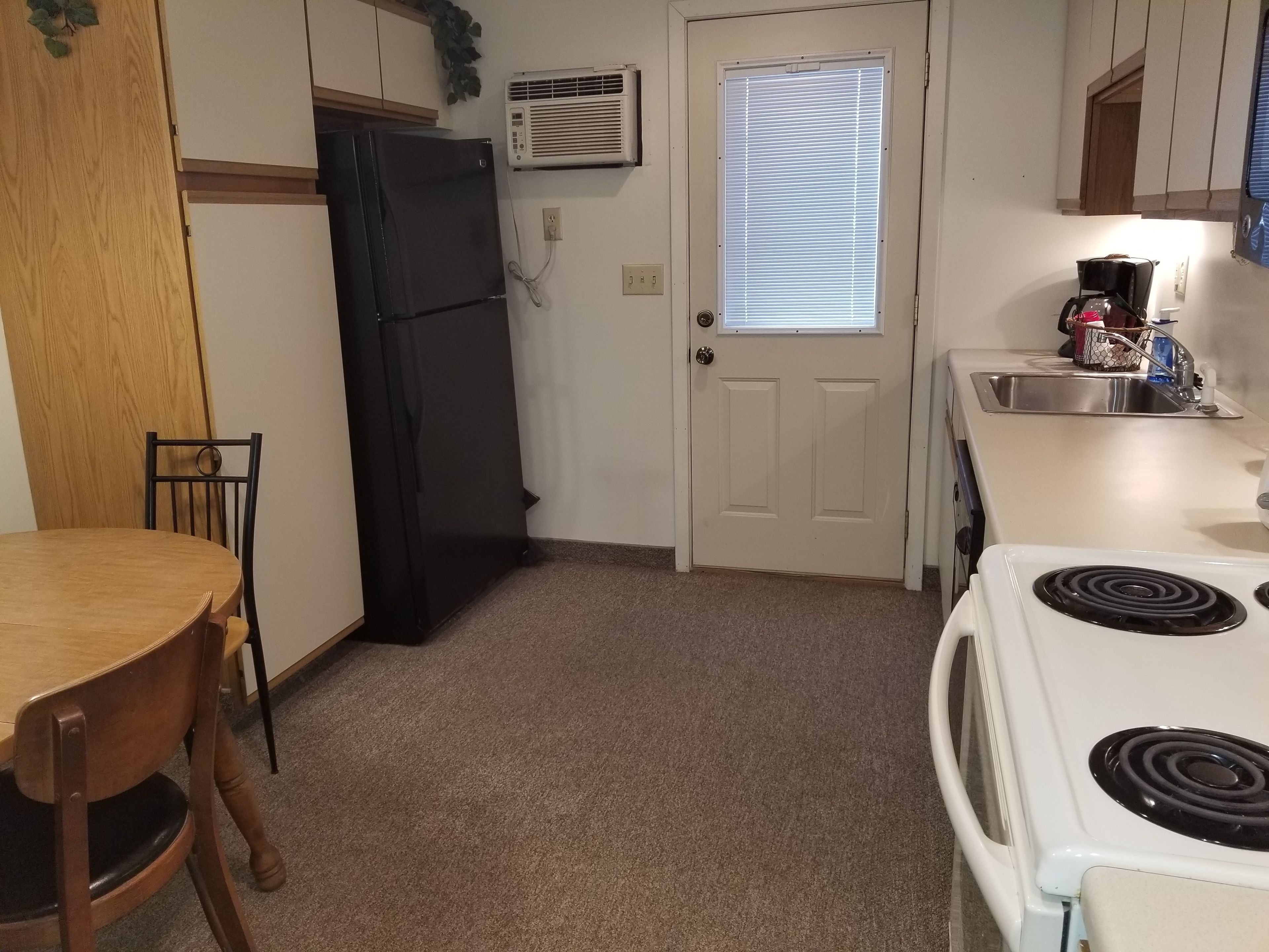 Cocina compacta con refrigerador, estufa, pileta y ventana con persianas.
