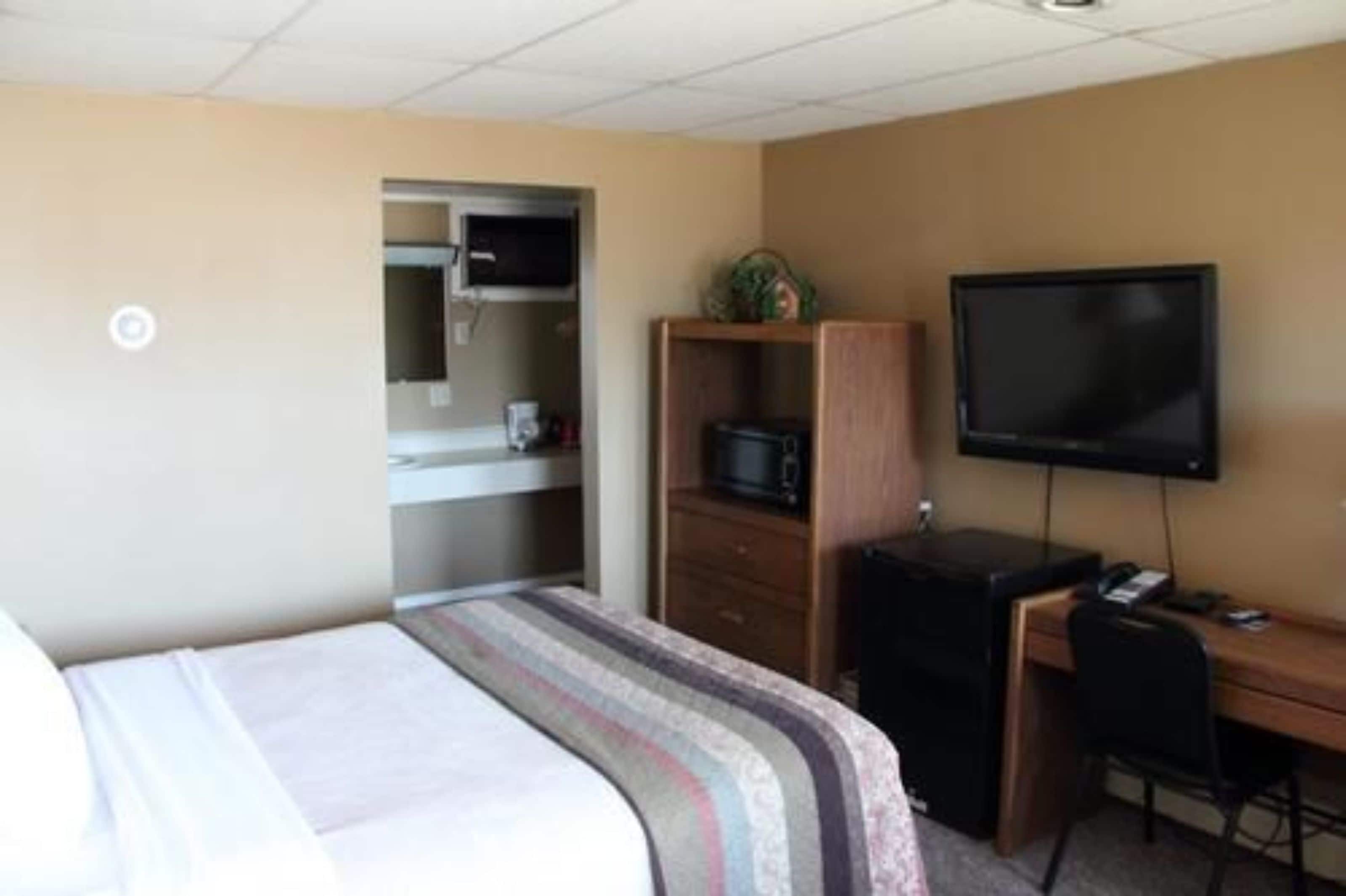 A hotel room with a bed, a desk with a computer, a television, and a microwave.