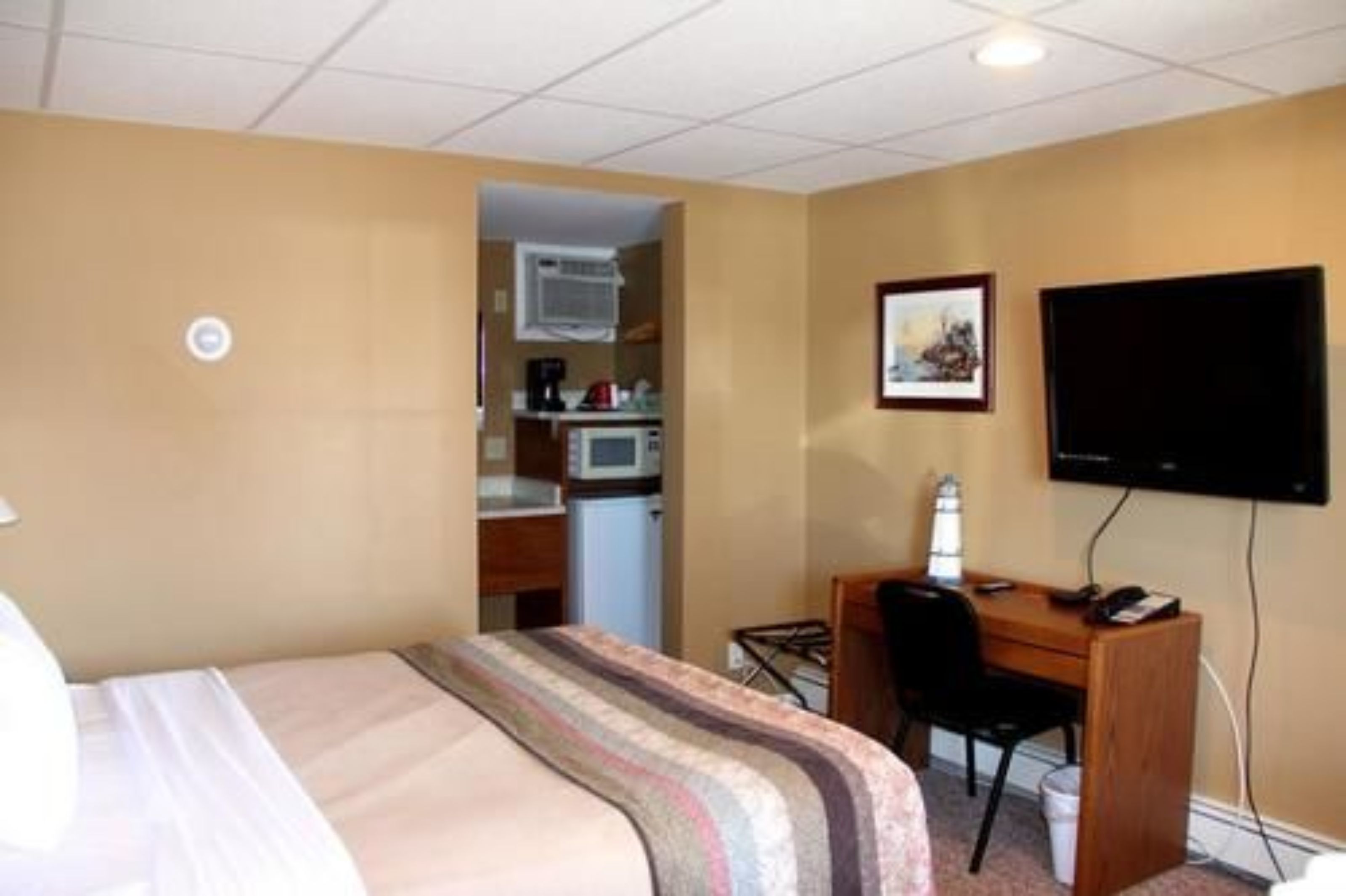 A hotel room with a bed, a desk, a chair, a television, and a kitchenette.