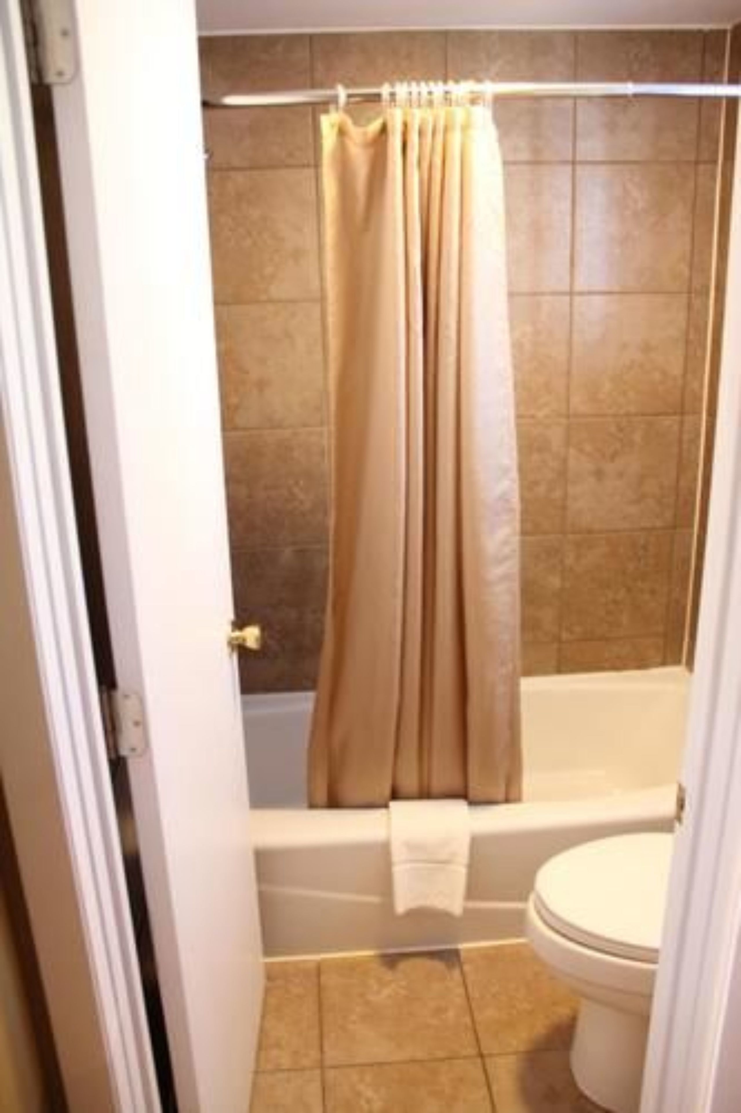 A bathroom with a bathtub, toilet, and beige tiles.