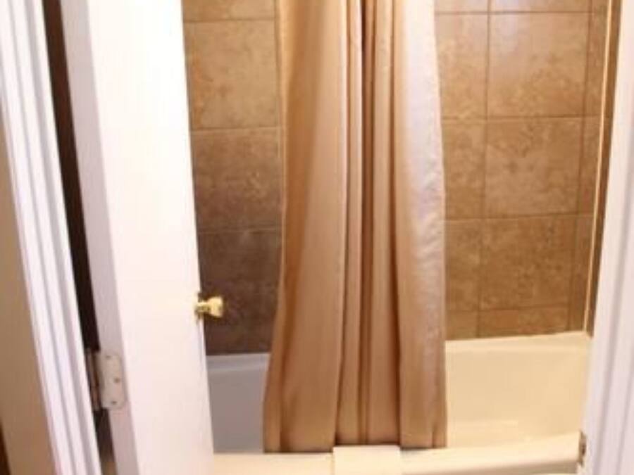 A bathroom with a bathtub, toilet, and beige tiles.