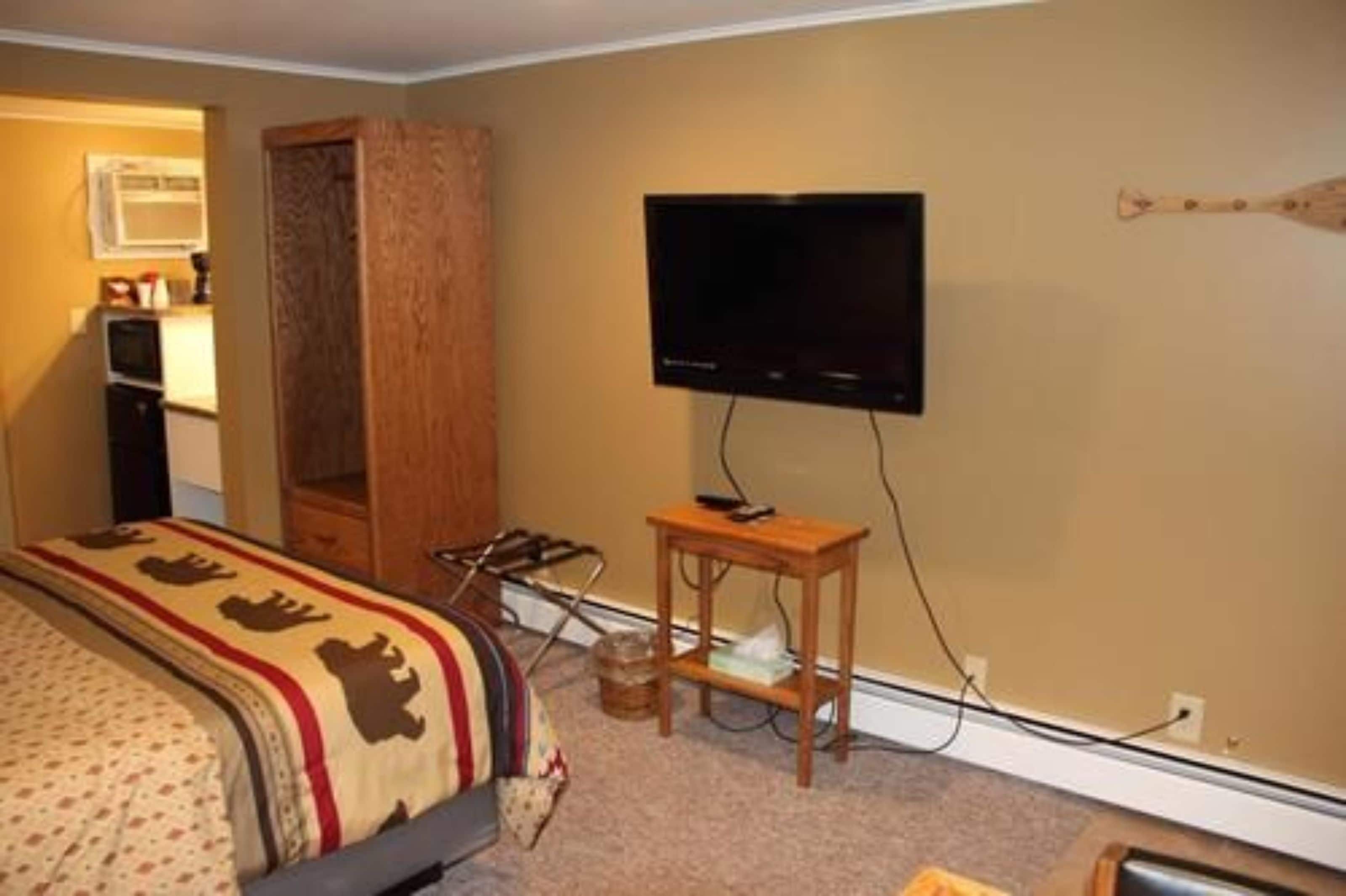 Een hotelkamer met een bed, een aan de muur bevestigde televisie en een houten garderobe.