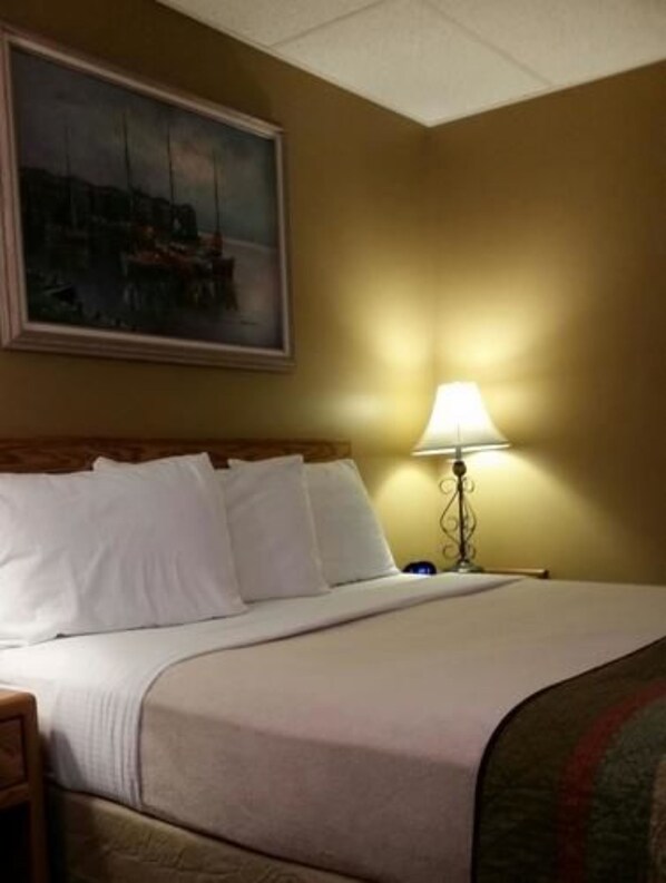 Quarto de hotel com cama, mesa de cabeceira, abajur e um quadro na parede.