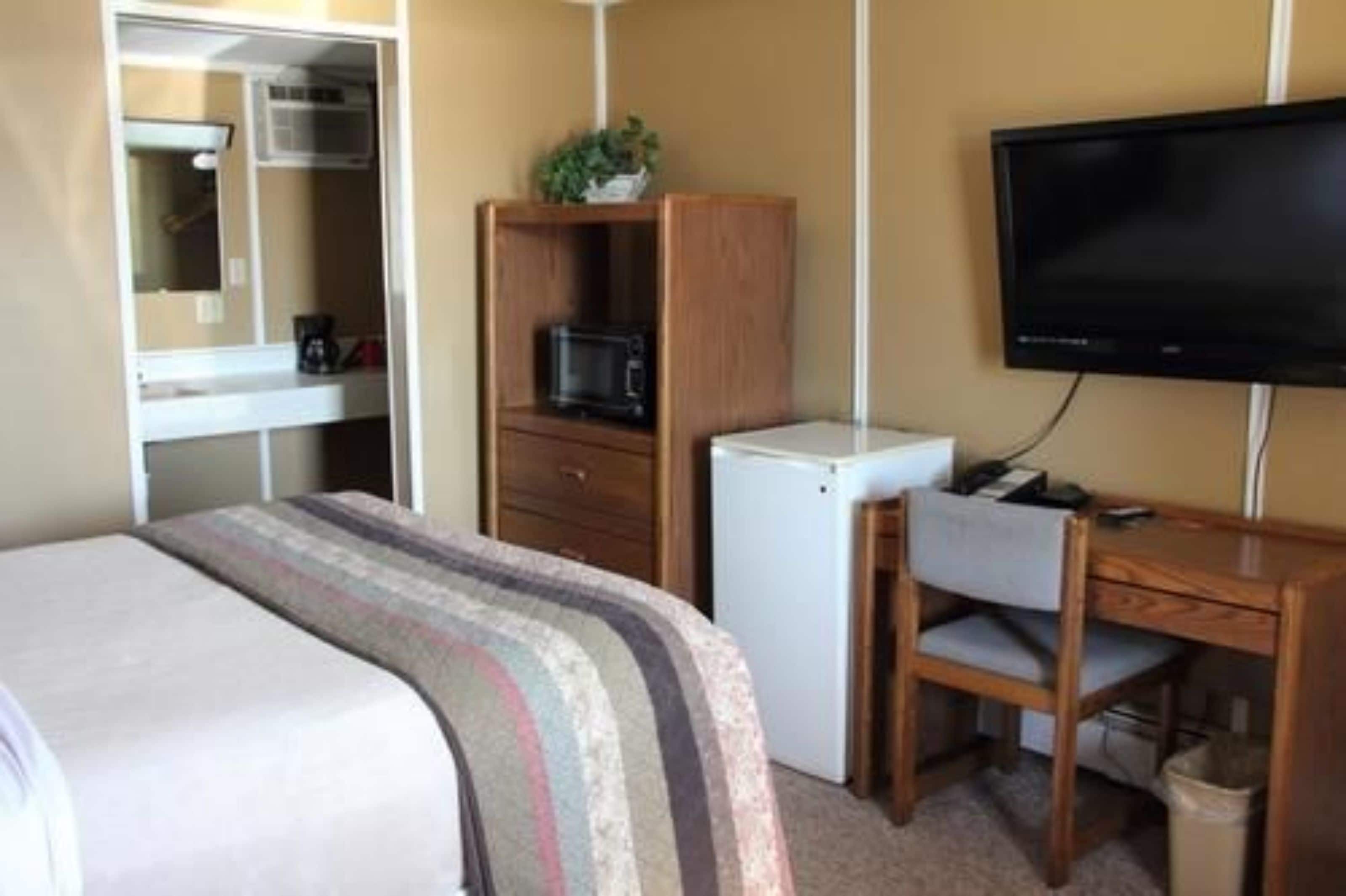 Quarto de hotel com cama, escrivaninha, cadeira, televisão, micro-ondas e frigorífico.