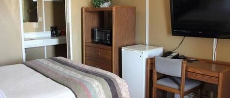 Quarto de hotel com cama, escrivaninha, cadeira, televisão, micro-ondas e frigorífico.