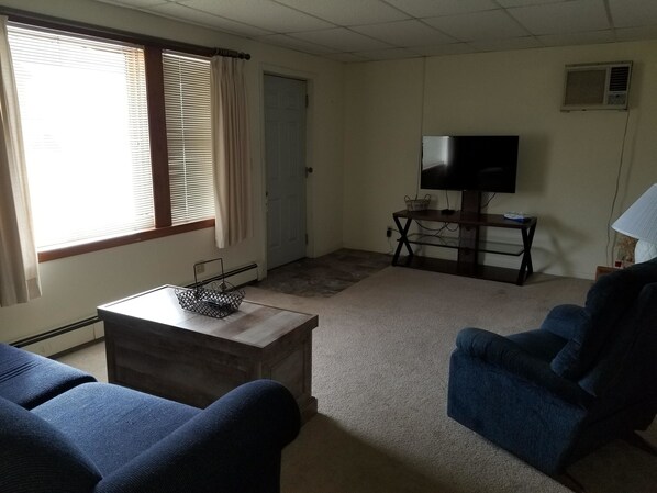 A living room with a blue sofa, a coffee table, a TV on a stand, and a door.