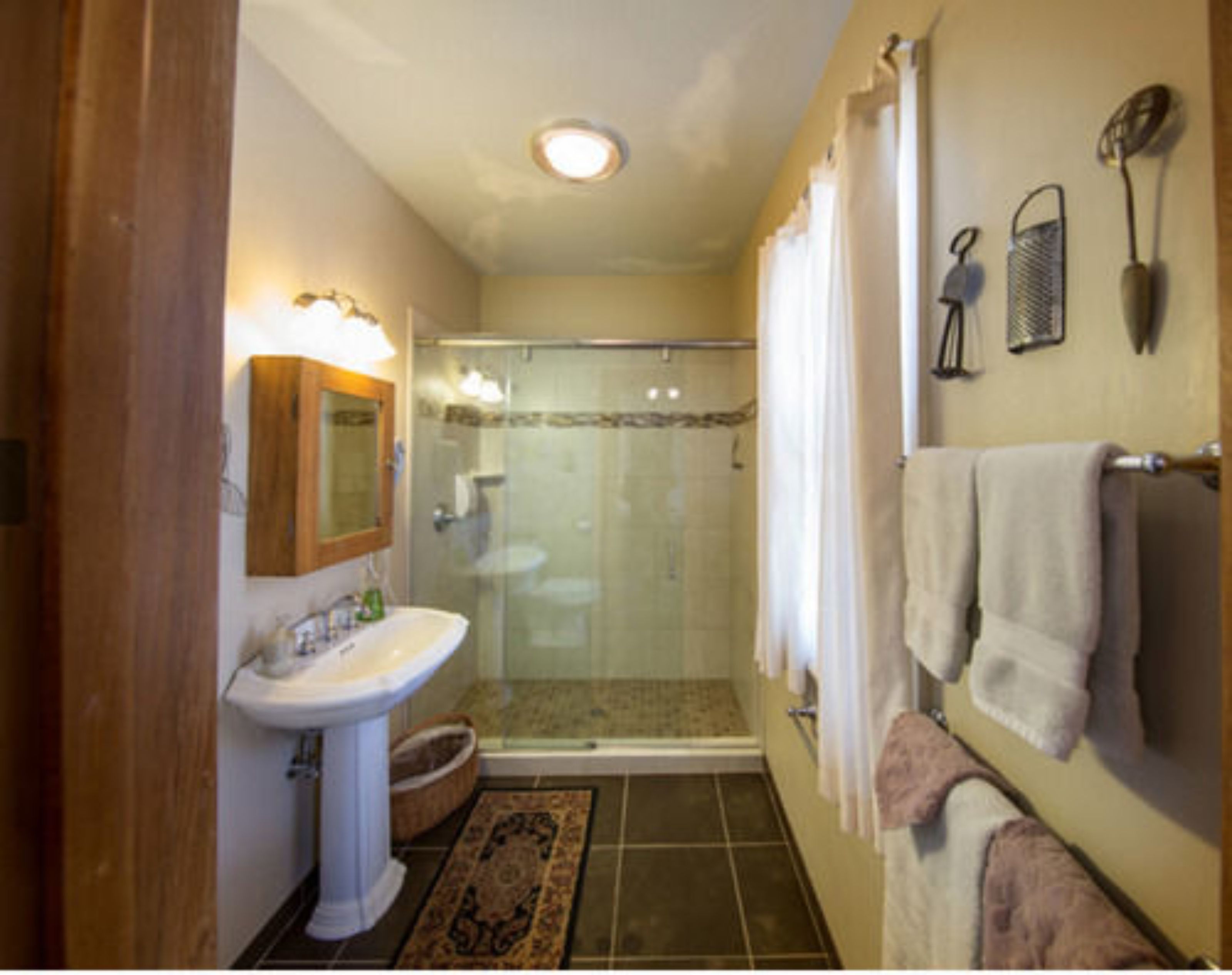 A bathroom with a glass shower enclosure, a pedestal sink, and a towel rack with multiple towels.