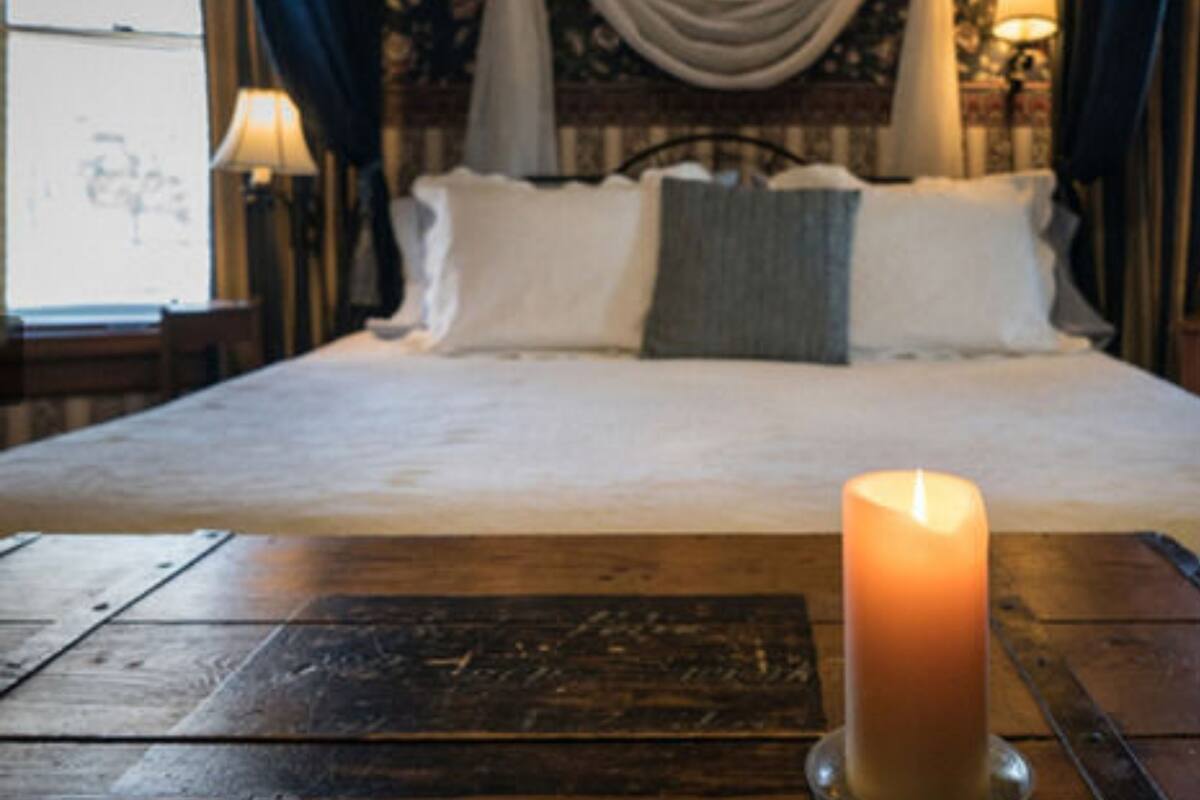 Un lit recouvert de draps blancs, une seule bougie allumée et une table en bois sombre placée devant.