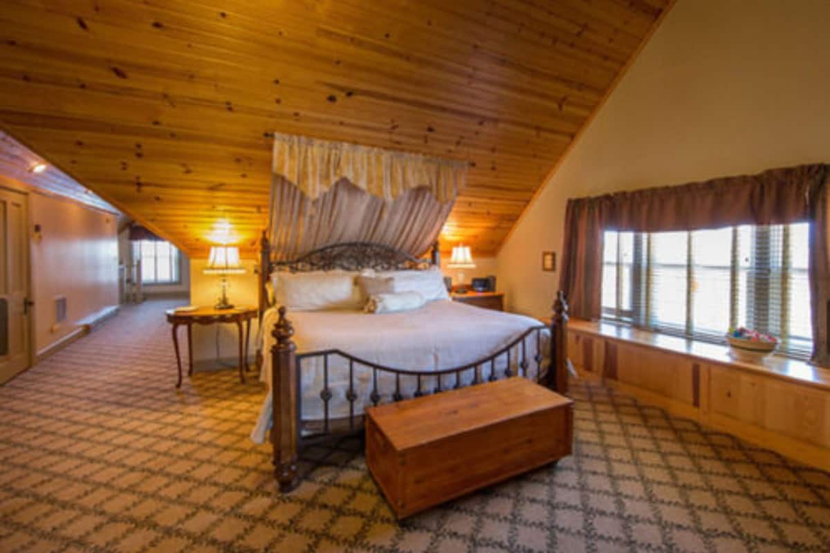 Une chambre avec un plafond en bois, un lit à baldaquin, deux tables de chevet et une fenêtre avec des rideaux.