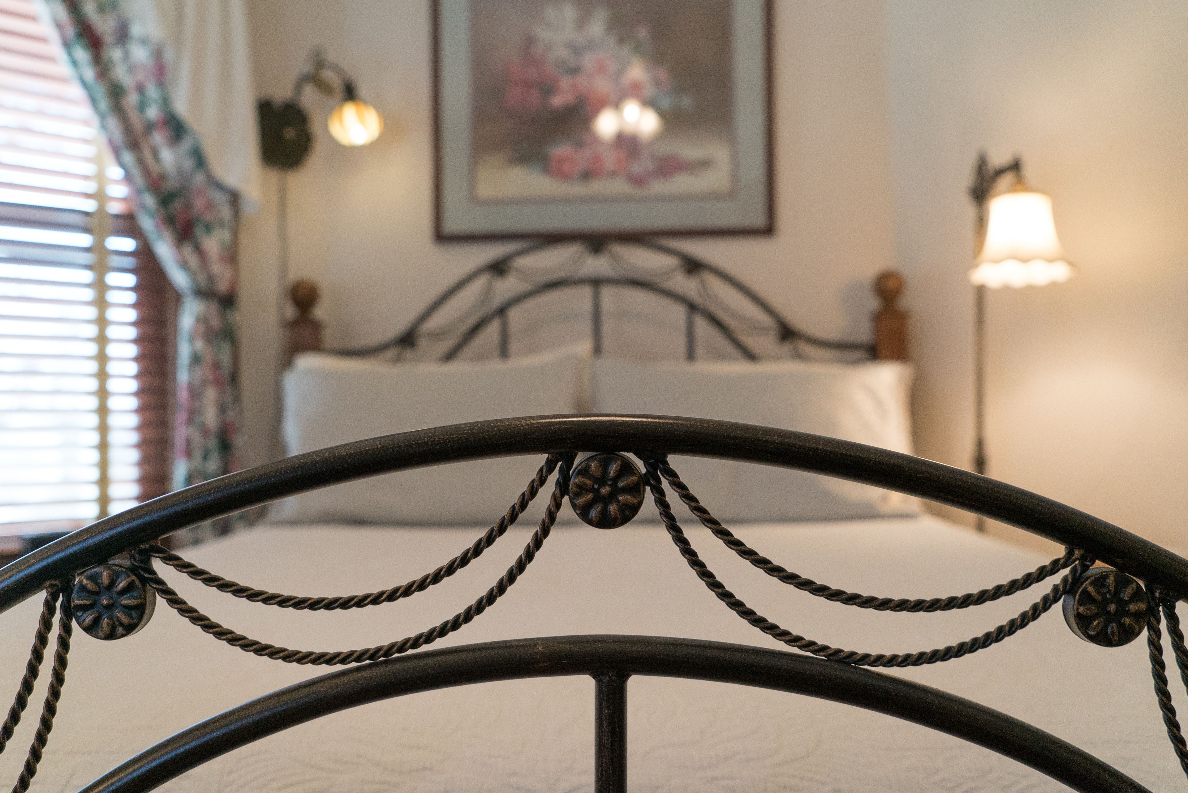Una cama con cabecera metálica en una habitación con un cuadro en la pared y dos lámparas fijadas a la pared.