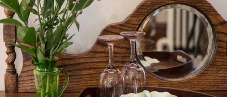 A wooden side table with a green vase containing flowers, a tray with a white bowl, and a mirror.