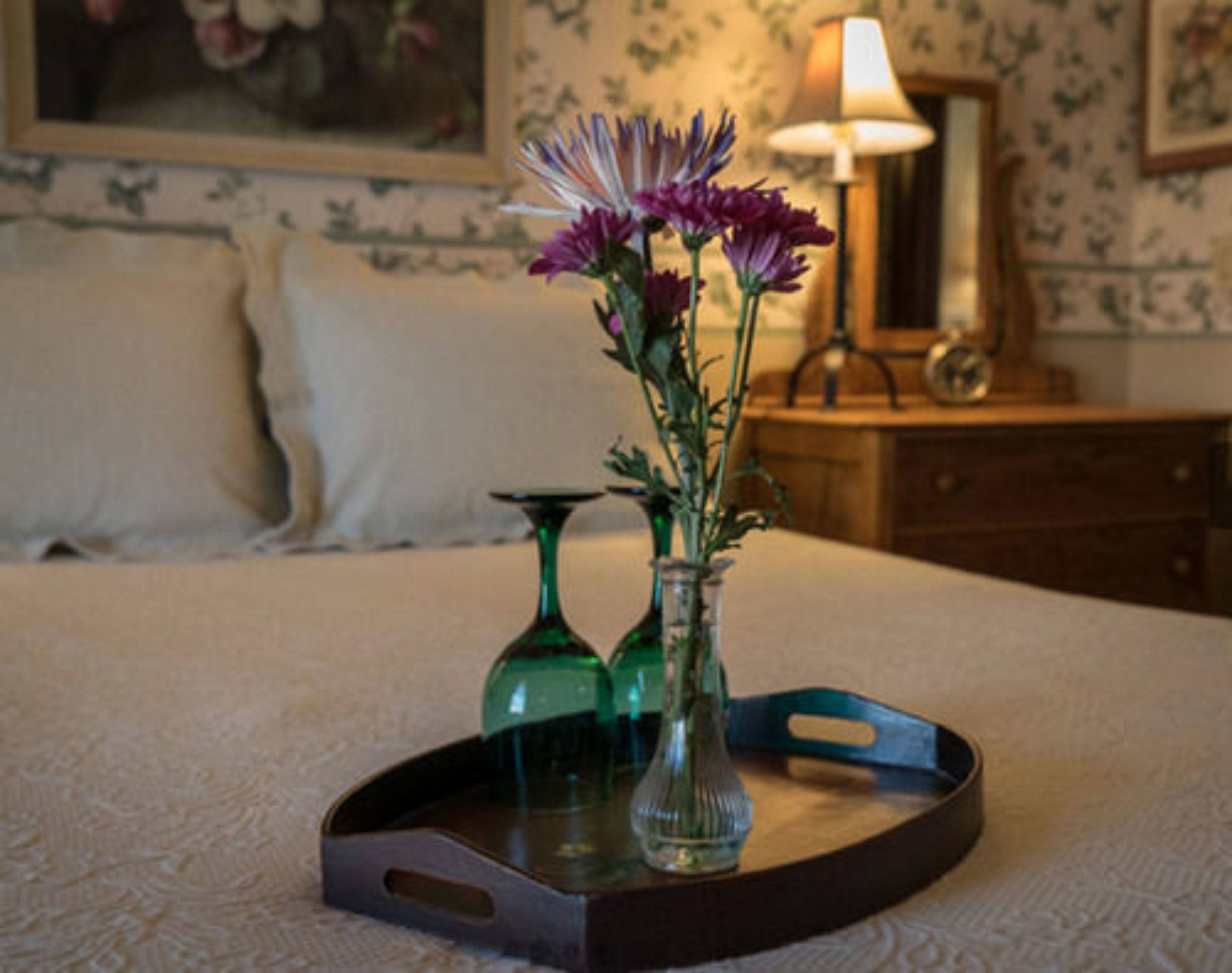 A bed with a tray holding a vase with flowers and a candle.