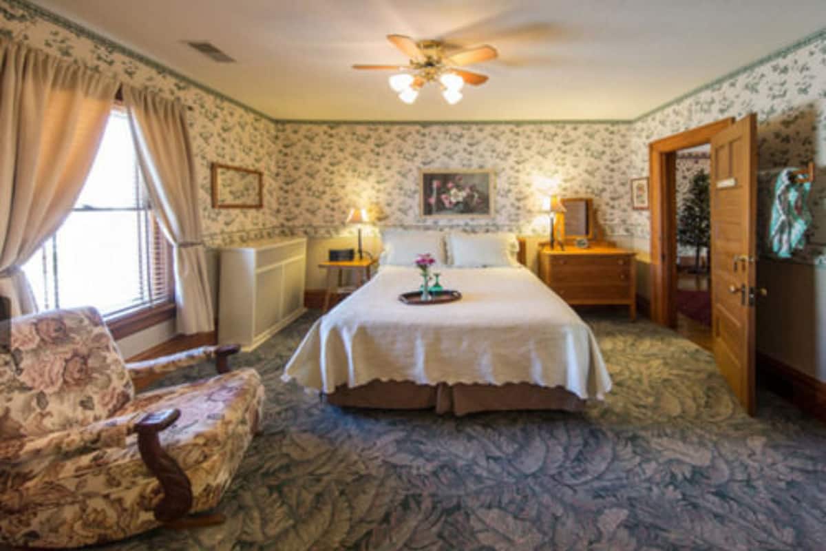 Une chambre à coucher avec un grand lit, une chaise, un ventilateur de plafond et une armoire en bois.