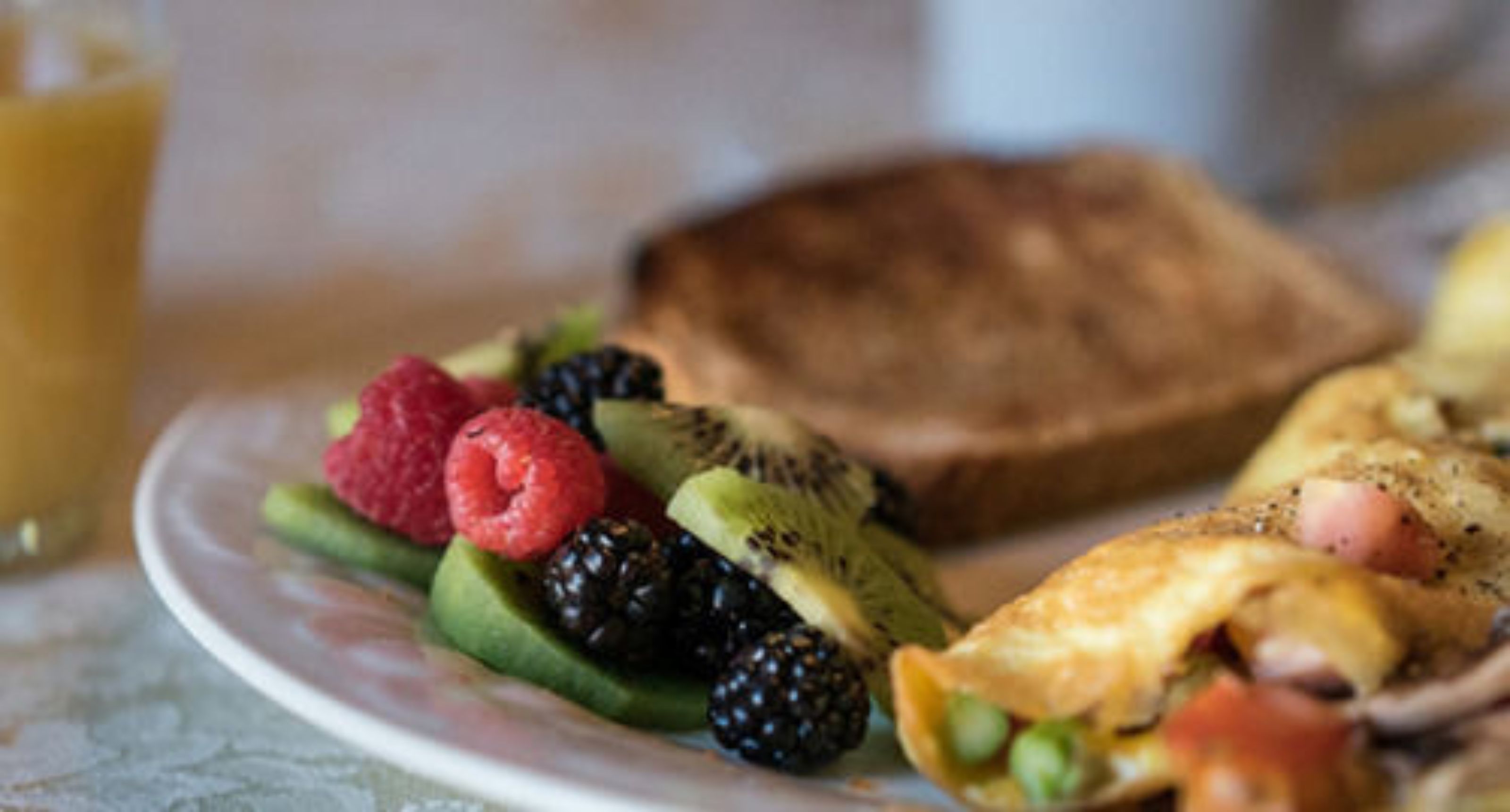 A plate with toast, scrambled eggs, and assorted fruits including kiwi, raspberries, and blackberries.