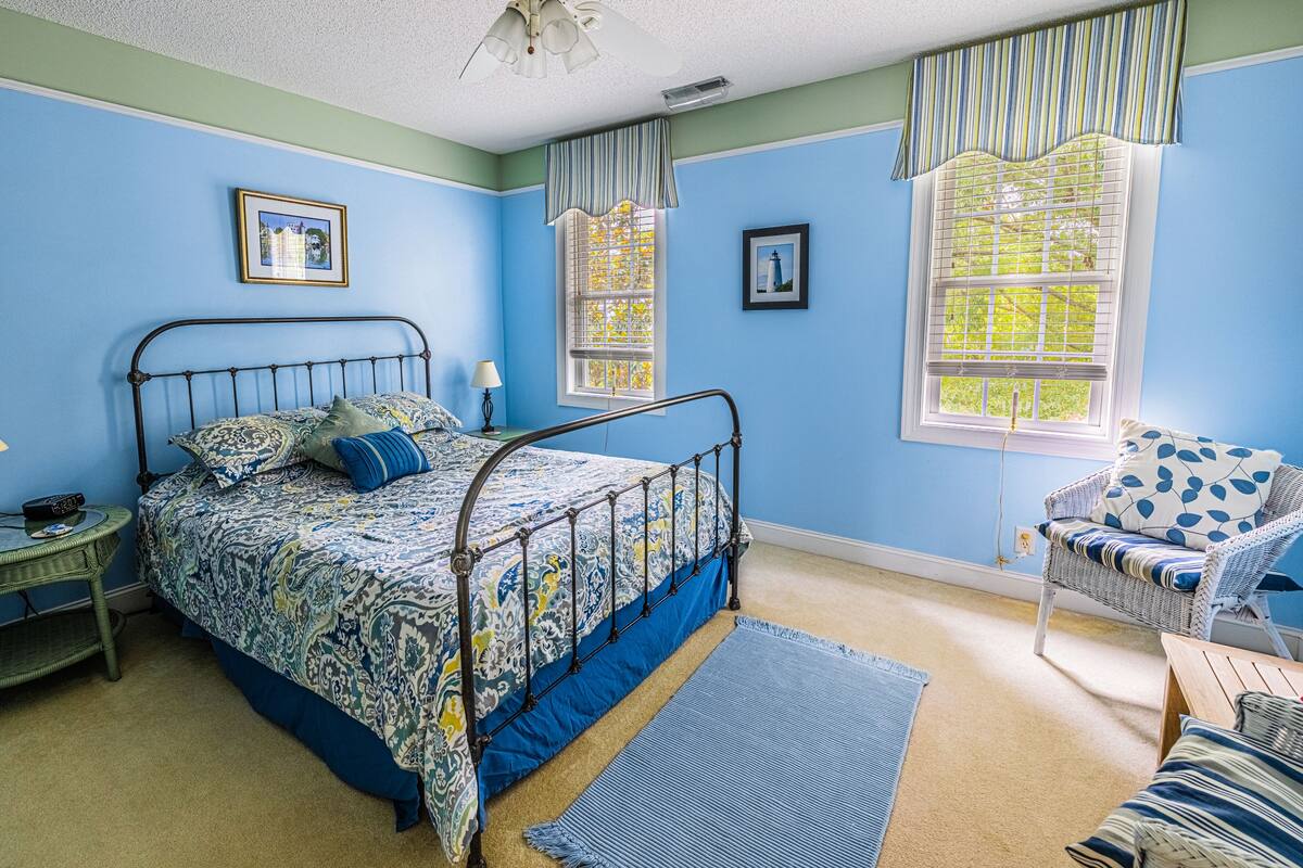 Quarto com cama, cadeira, mesa de cabeceira e janela com persianas.