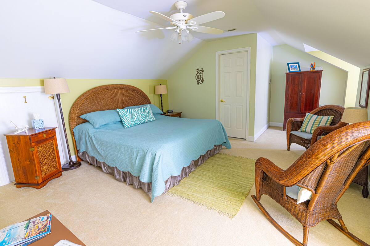 Quarto com cama, poltrona de balanço, mesa de cabeceira, luminária e porta.