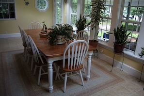 A dining area with a wooden table, white chairs, and potted plants. - The Inn on Bath Creek (Bath)