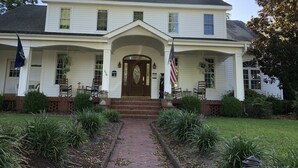 A two-story white house with a central entrance, a porch with chairs, and an American flag. - The Inn on Bath Creek (Bath)