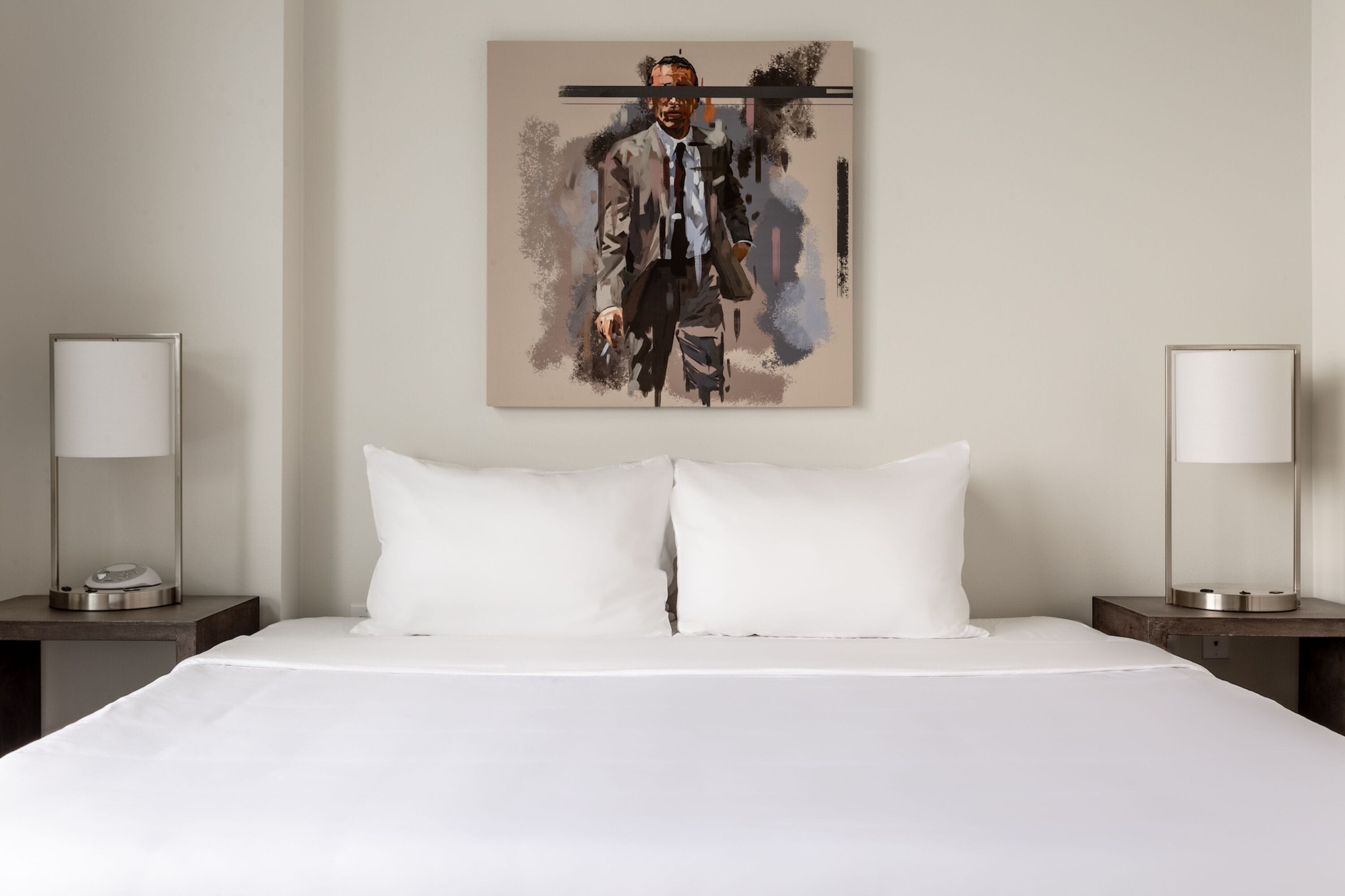 Ein Hotelzimmer mit einem großen Bett, weißer Bettwäsche, zwei Nachttischen mit Lampen und einem Wandbild.