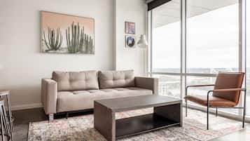 Una sala moderna con un sofá, una mesa de centro y un sillón. Se ve una ventana grande que ofrece vistas a la ciudad.