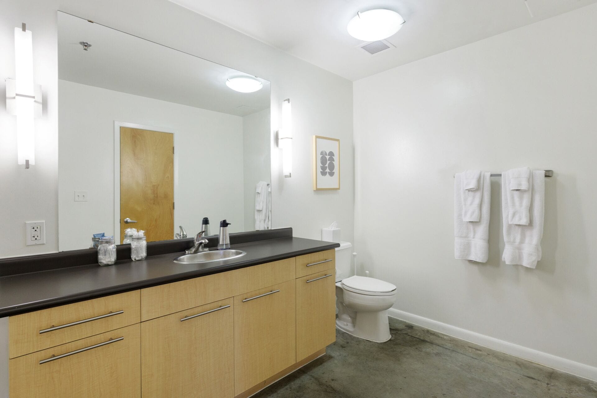 A bathroom with a large mirror, a sink, a toilet, and a towel rack.