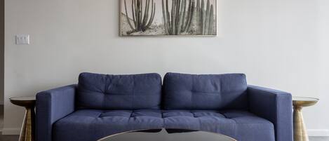 A blue sofa against a white wall with a cactus painting above it.