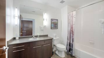 A modern bathroom with a wooden vanity, a toilet, a shower with a curtain, and a large mirror.