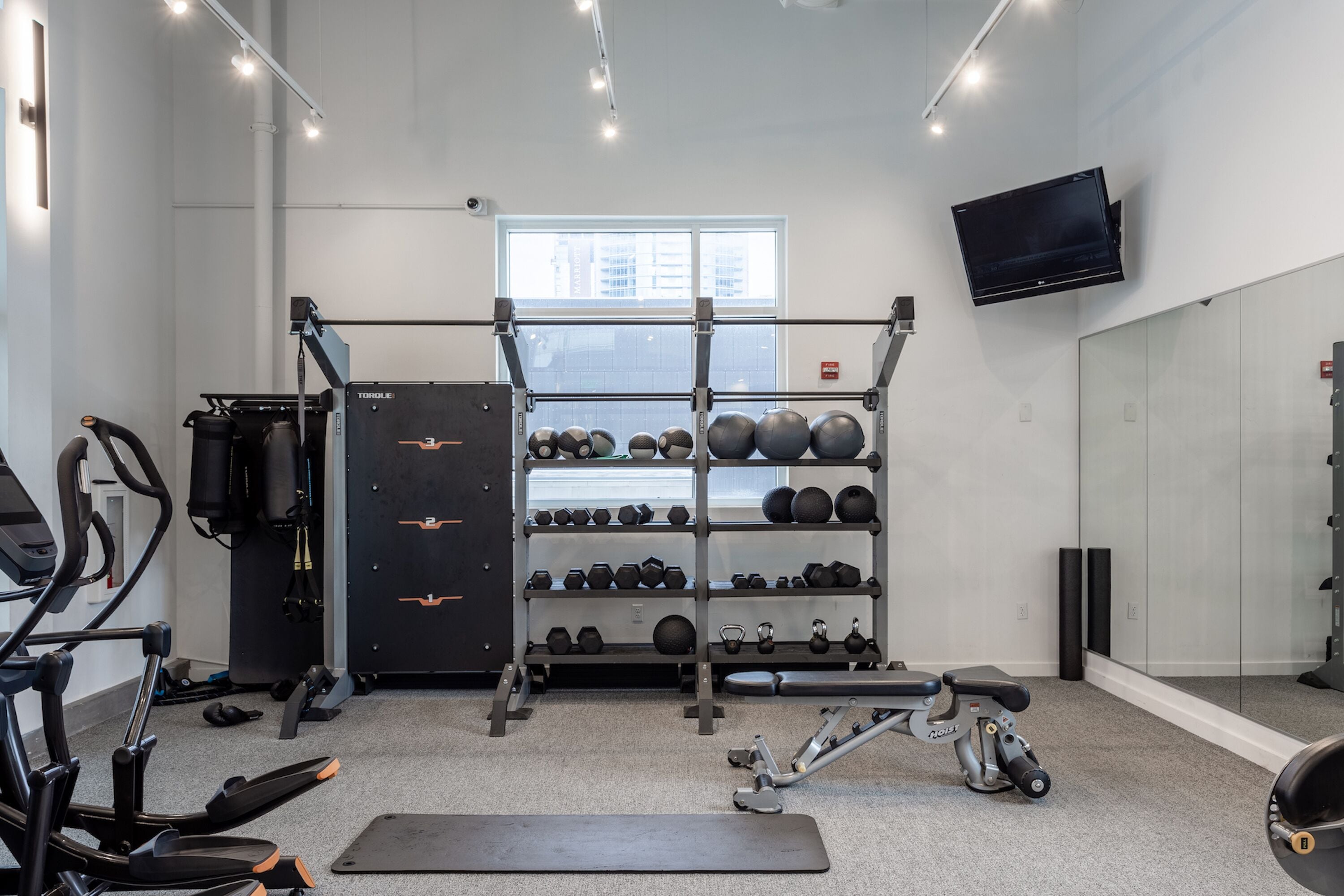 A gym with exercise equipment, a squat rack, and a wall-mounted TV.