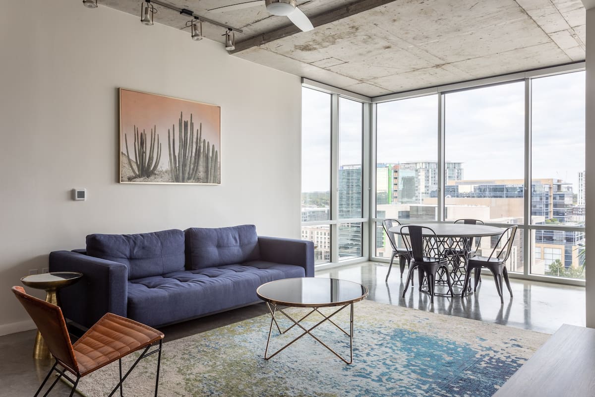 Ein moderner Arbeitsbereich mit einem blauen Sofa, einem runden Glastisch und Blick auf die Stadt durch große Fenster.