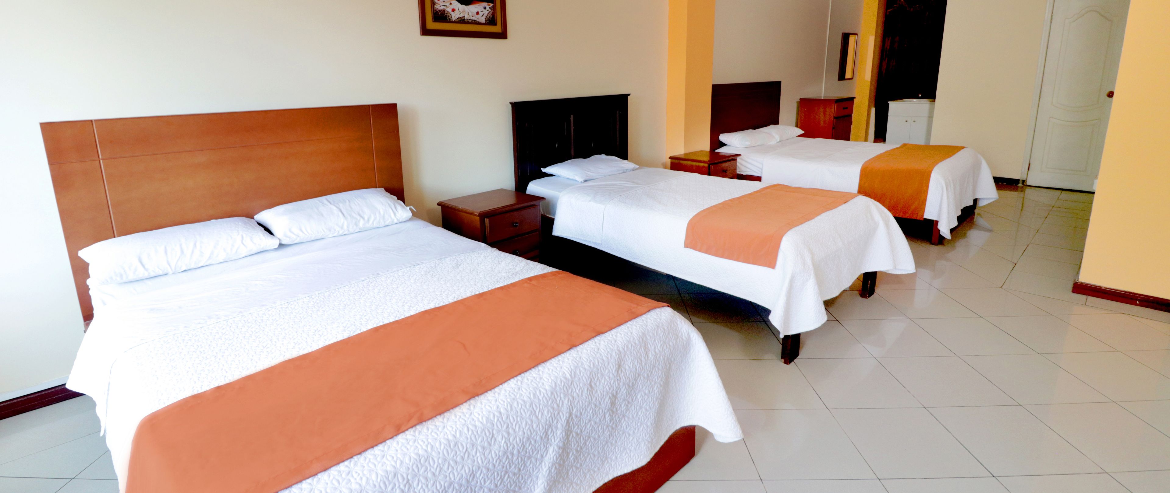 Une chambre d’hôtel avec deux lits, chacun agrémenté de draps blancs et de touches de couleur orange, une tête de lit en bois, une petite table de chevet et un téléviseur.