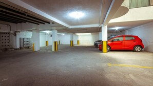 Een parkeergarage met betonnen vloeren, gele pilaren en een rode auto die in een van de parkeerplaatsen staat.
