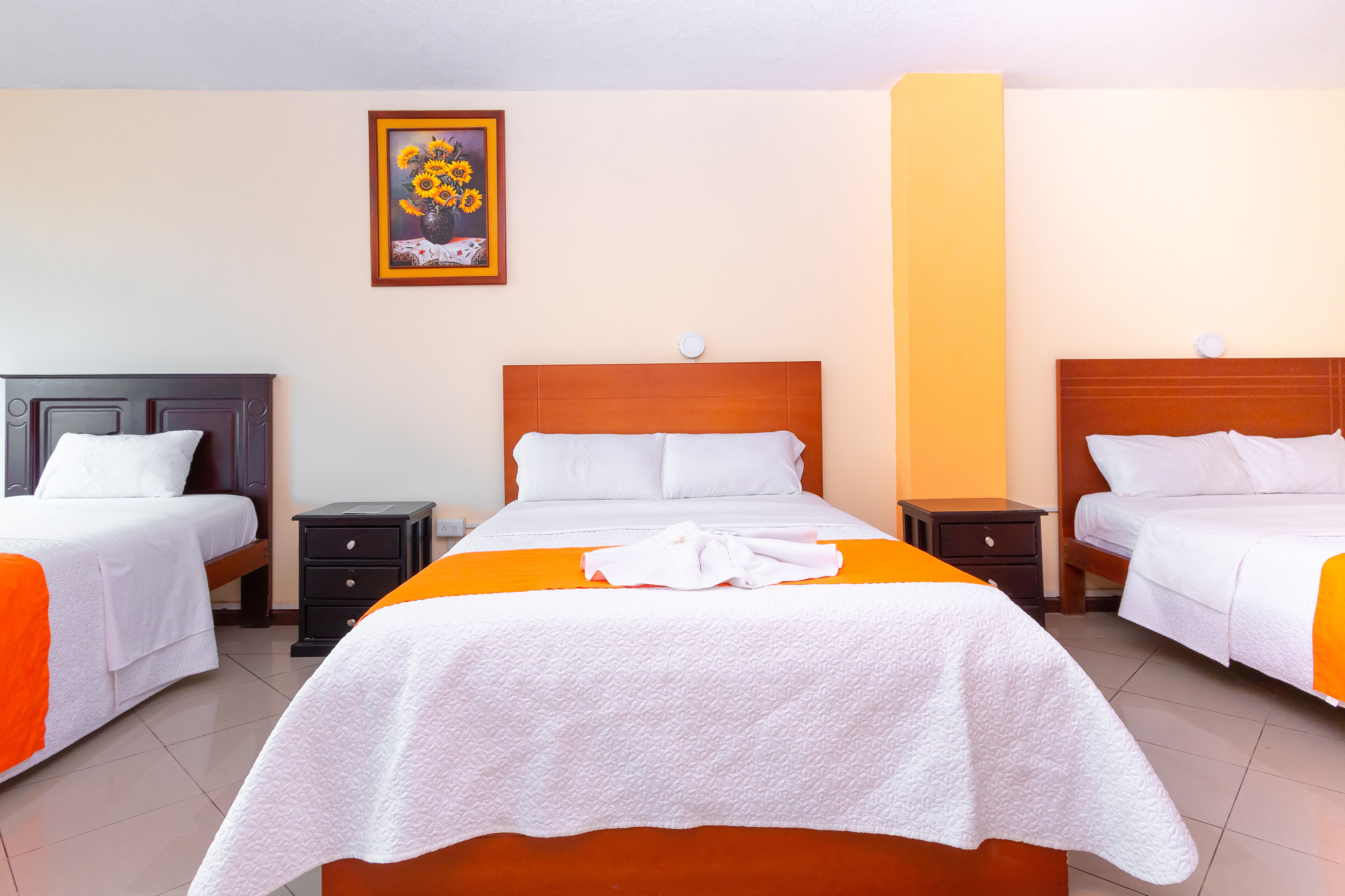 Une chambre d’hôtel avec deux lits, une table de chevet, un tableau encadré au mur et une serviette blanche sur chaque lit.