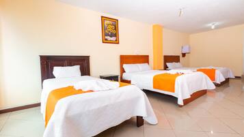 A hotel room with three beds, each with white bedding and orange accents, a wooden headboard, and a painting of sunflowers on the wall.