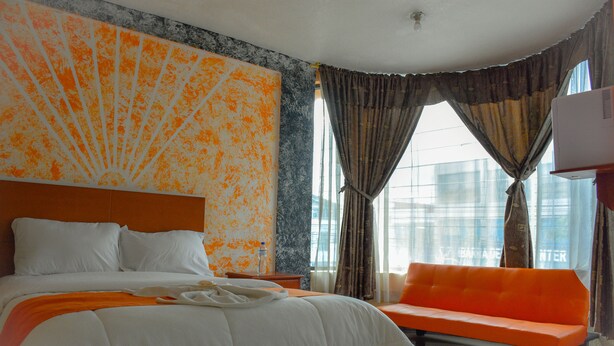 Een hotelkamer met een groot bed, een oranje bank en uitzicht op de stad door grote ramen.